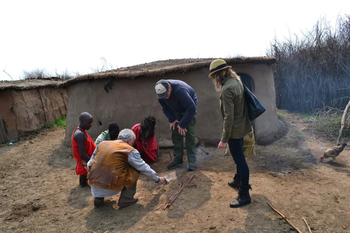 A visitor kneeling beside Maasai men as they start a fire with sticks