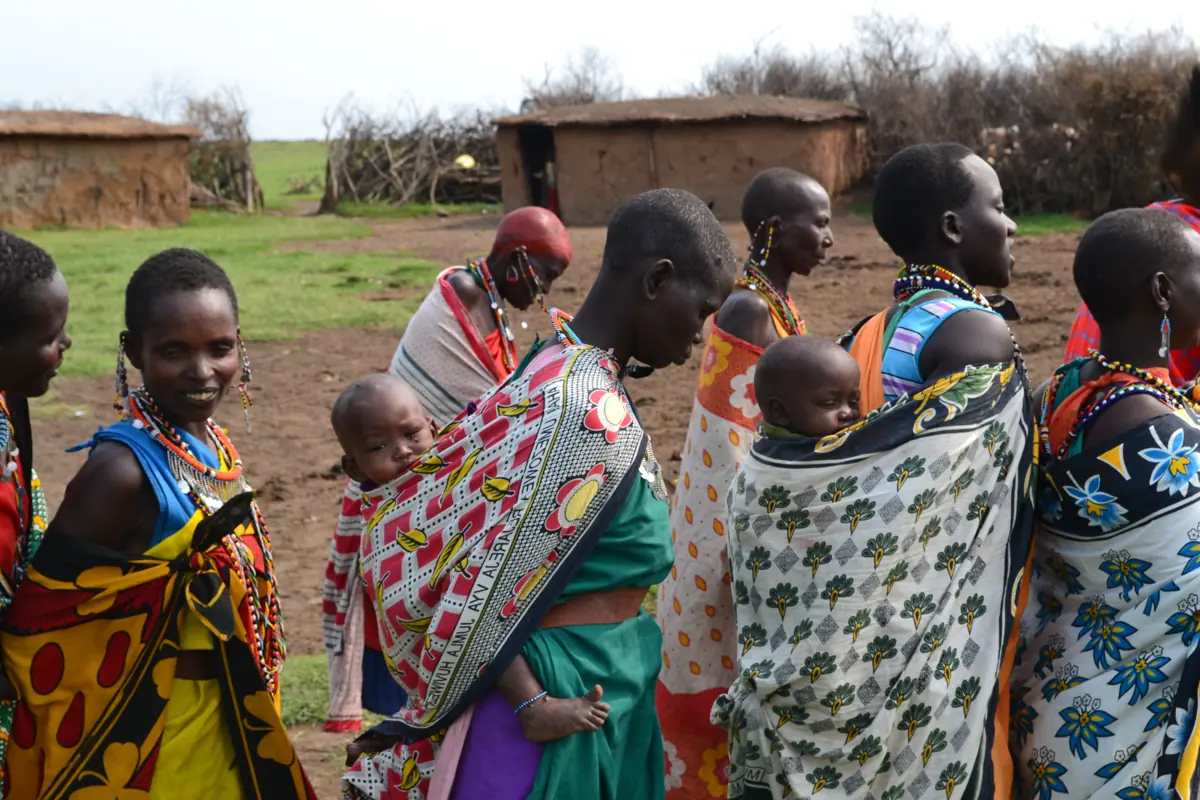 Maasai women in brightly patterned cloths standing together in their village